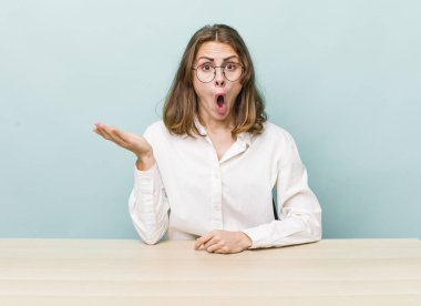 Genç ve güzel bir kadın şaşırmış ve şok olmuş görünüyor. Çenesi düşmüş ve elinde bir nesne tutuyor. masa ve iş konsepti