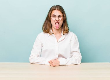 Genç ve güzel bir kadın iğreniyor, sinirleniyor ve dilini çıkarıyor. masa ve iş konsepti