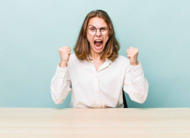 Genç ve güzel bir kadın sinirli bir ifadeyle agresif bir şekilde bağırıyor. masa ve iş konsepti