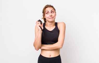 Genç, güzel bir kadın omuz silkiyor, kafası karışık ve kararsız. fitness konsepti ve kronometre