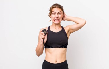 Genç ve güzel bir kadın gergin, endişeli ya da korkmuş hissediyor. Elleri başının üstünde. fitness konsepti ve kronometre