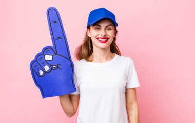 Genç ve güzel bir kadın mutlu bir şekilde gülümsüyor, eli kalçasında ve kendinden emin. Bir numaralı hayran konsepti