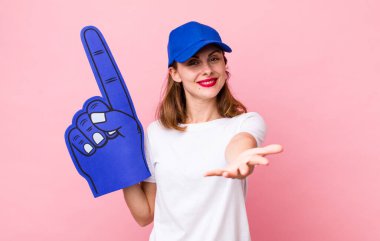 Genç ve güzel bir kadın arkadaşça gülümsüyor ve bir konsept sunuyor. Bir numaralı hayran konsepti