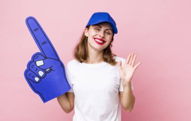 Genç ve güzel bir bayan mutlu bir şekilde gülümsüyor, el sallıyor, sizi selamlıyor ve selamlıyor. Bir numaralı hayran konsepti