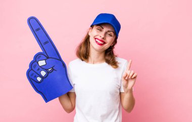 Genç, güzel bir bayan gülümsüyor ve arkadaş canlısı görünüyor. Bir numarayı gösteriyor. Bir numaralı hayran konsepti