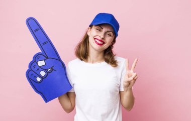 Genç, güzel bir bayan gülümsüyor ve iki numarayı gösteriyor. Bir numaralı hayran konsepti