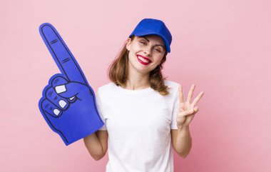 Genç, güzel bir bayan gülümsüyor ve arkadaş canlısı görünüyor, üç numarayı gösteriyor. Bir numaralı hayran konsepti