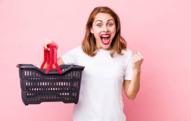 Genç ve güzel bir kadın şokta, gülüyor ve başarıyı kutluyor. boş alışveriş sepeti kavramı