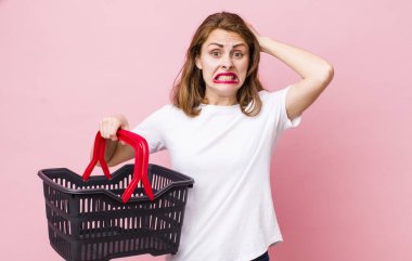 Genç ve güzel bir kadın gergin, endişeli ya da korkmuş hissediyor. Elleri başının üstünde. boş alışveriş sepeti kavramı