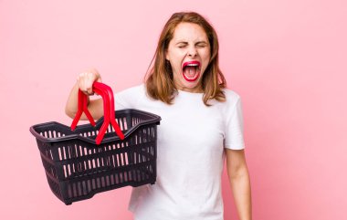 Genç ve güzel bir kadın agresif bir şekilde bağırıyor, çok kızgın görünüyor. boş alışveriş sepeti kavramı