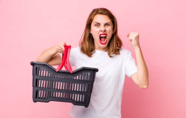 Genç ve güzel bir kadın sinirli bir ifadeyle agresif bir şekilde bağırıyor. boş alışveriş sepeti kavramı