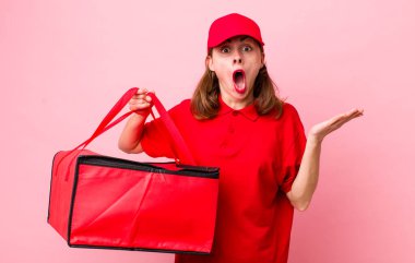 Genç ve güzel bir kadın şaşırmış ve şok olmuş görünüyor. Çenesi düşmüş ve elinde bir nesne tutuyor. Pizza teslimatı kavramı
