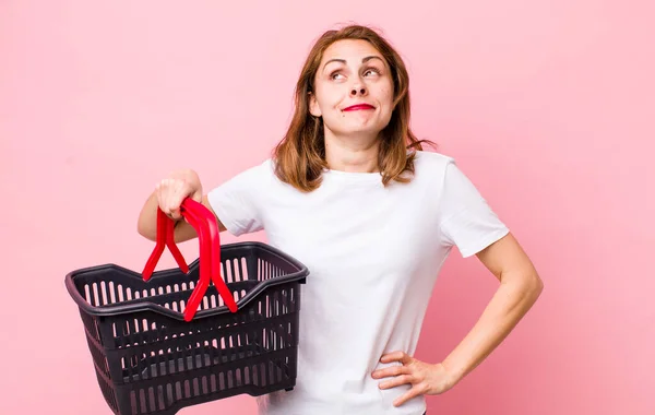 Young Pretty Woman Shrugging Feeling Confused Uncertain Empty Shopping Basket — Stockfoto