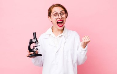 Genç ve güzel bir kadın şokta, gülüyor ve başarıyı kutluyor. Mikroskop konseptine sahip bilim adamı