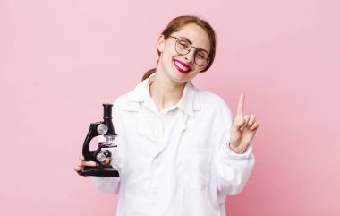 Genç, güzel bir bayan gülümsüyor ve arkadaş canlısı görünüyor. Bir numarayı gösteriyor. Mikroskop konseptine sahip bilim adamı