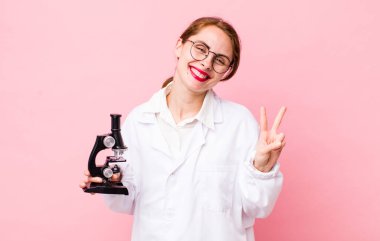 Genç, güzel bir bayan gülümsüyor ve iki numarayı gösteriyor. Mikroskop konseptine sahip bilim adamı