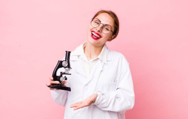 Genç, güzel bir kadın neşeyle gülümsüyor, mutlu hissediyor ve bir konsept gösteriyor. Mikroskop konseptine sahip bilim adamı
