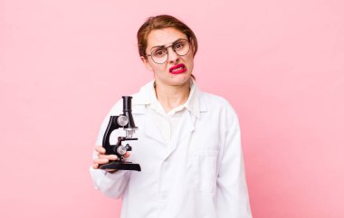 Genç ve güzel bir kadın şaşkın ve şaşkın hissediyor. Mikroskop konseptine sahip bilim adamı