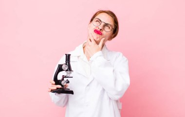 Genç, güzel bir kadın düşünüyor, kuşkulu ve şaşkın hissediyor. Mikroskop konseptine sahip bilim adamı