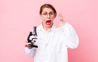 Genç ve güzel bir kadın ellerini havaya kaldırarak çığlık atıyor. Mikroskop konseptine sahip bilim adamı