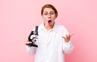 Genç ve güzel bir kadın şok olmuş ve şaşırmış hissediyor. Mikroskop konseptine sahip bilim adamı