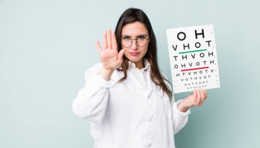 young pretty woman  looking serious showing open palm making stop gesture. optical vision test concept