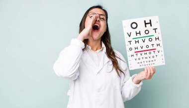 young pretty woman  feeling happy,giving a big shout out with hands next to mouth. optical vision test concept
