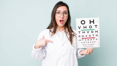 young pretty woman  looking shocked and surprised with mouth wide open, pointing to self. optical vision test concept