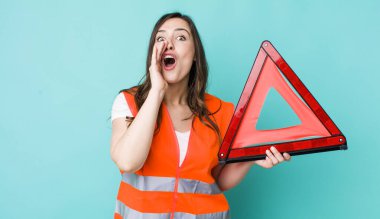 young pretty woman  feeling happy,giving a big shout out with hands next to mouth. car emergency triangle