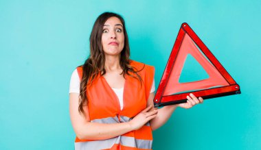 young pretty woman  shrugging, feeling confused and uncertain. car emergency triangle