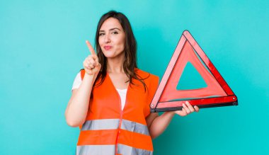 young pretty woman  smiling and looking friendly, showing number one. car emergency triangle