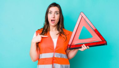 young pretty woman  looking shocked and surprised with mouth wide open, pointing to self. car emergency triangle