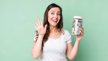 Genç ve güzel bir bayan mutlu bir şekilde gülümsüyor, el sallıyor, sizi selamlıyor ve selamlıyor. kaydetme kavramı