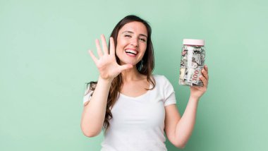 Genç, güzel bir bayan gülümsüyor ve arkadaş canlısı görünüyor, beş numarayı gösteriyor. kaydetme kavramı