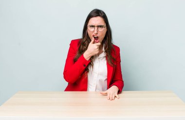 Ağzı ve gözleri açık, eli çenesinde genç ve güzel bir kadın. iş kavramı