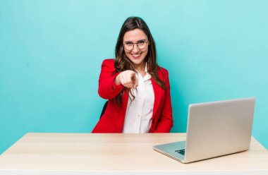 young pretty woman  pointing at camera choosing you. business desk concept