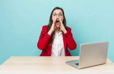 young pretty woman  feeling happy,giving a big shout out with hands next to mouth. business desk concept
