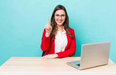 young pretty woman  smiling and looking friendly, showing number one. business desk concept