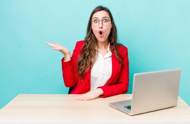 young pretty woman  looking surprised and shocked, with jaw dropped holding an object. business desk concept