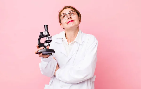 young pretty woman  shrugging, feeling confused and uncertain. scientist with microscope concept
