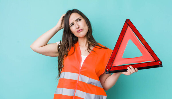 young pretty woman  feeling puzzled and confused, scratching head. car emergency triangle