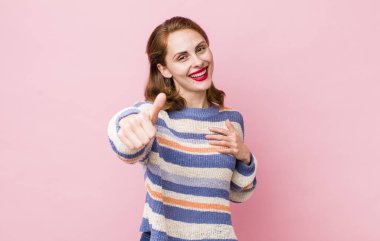 Genç, güzel bir kadın gururlu, tasasız, kendinden emin ve mutlu, başparmağıyla olumlu gülümsüyor.