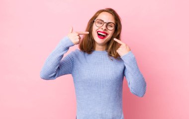 Genç, güzel bir kadın, kendine güvenerek gülümsüyor. Kendi gülüşünü gösteriyor. Olumlu, rahat, tatmin olmuş bir tavır.