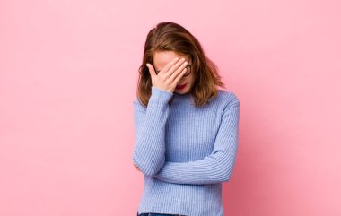 Genç, güzel bir kadın stresli, utanmış ya da üzgün görünüyor. Baş ağrısı var, yüzü elle kapatılmış.