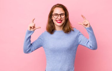 Genç, güzel bir kadın iki eliyle kendi gülüşünü çiziyor, olumlu ve mutlu görünüyor, sağIık kavramı.