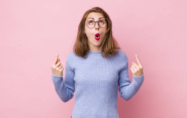 Genç ve güzel bir kadın huşu içinde ve ağzı açık bir şekilde şaşkın ve şaşkın bir bakışla yukarıya bakıyor.