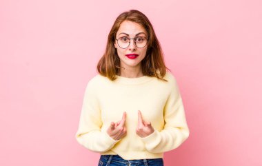 Genç ve güzel bir kadın, şaşkın ve şaşkın bir bakışla kendini işaret ediyor, seçildiğine şaşırmış ve şaşırmış.
