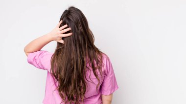 Genç, güzel bir kadın düşünüyor ya da şüphe ediyor, kafasını kaşıyor, kafası karışık ve kafası karışık hissediyor, geriye ya da arkaya bakıyor.