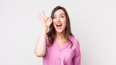 Genç ve güzel bir kadın kendini başarılı ve tatmin olmuş hissediyor, ağzı açık gülümsüyor, elle işaret veriyor.