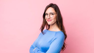 Genç ve güzel bir kadın kameraya çapraz kollarıyla gülümsüyor ve mutlu, kendinden emin, tatmin olmuş bir ifade, yan bakış.